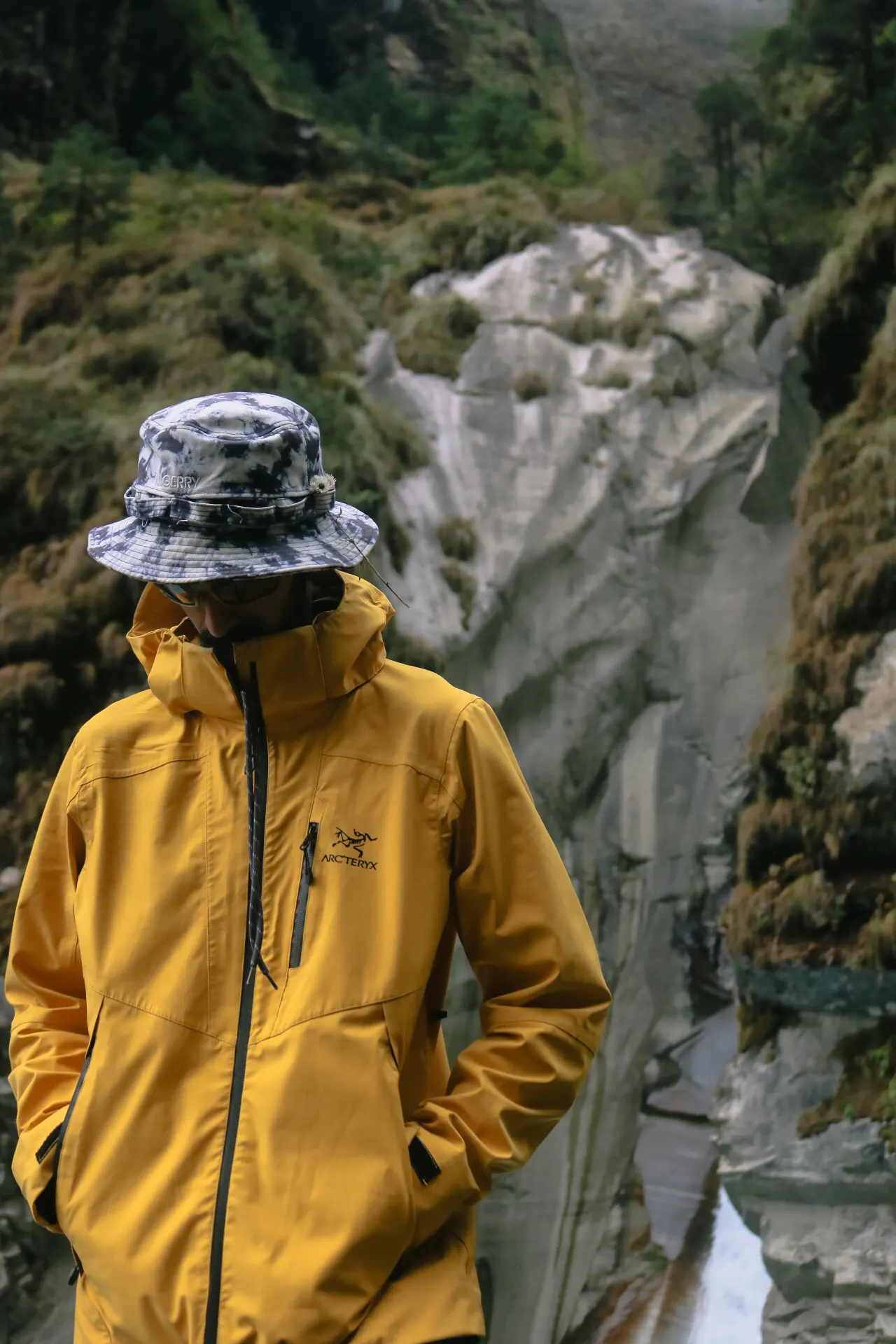 Person in a yellow rain jacket beside a mountain waterfall